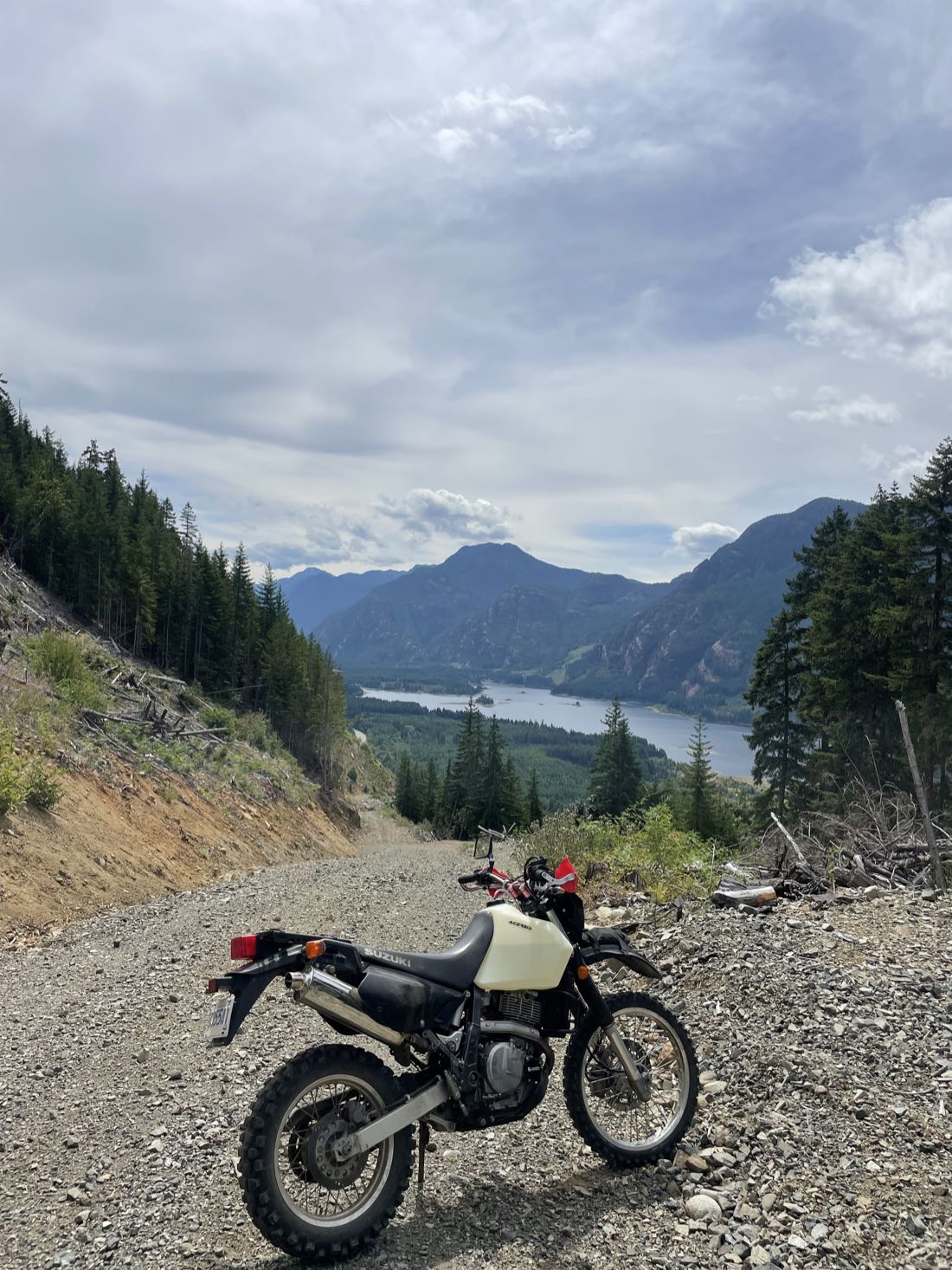 Dual-sport motorcycle on a high logging road switchback overlooking an inlet and coastal mountains on Vancouver Island